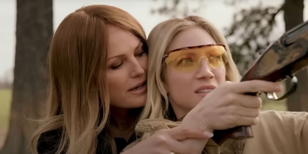 A still from the Hunting Wives trailer showing Brittany Snow in goggles while Malin Åkerman teaches her how to use a gun.
