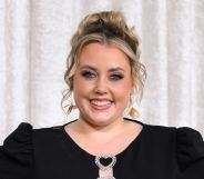 Charley Marlowe poses and smiles while wearing a black dress. She is stood against a white curtain background.