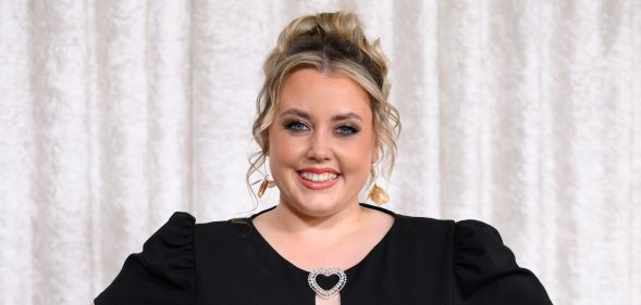 Charley Marlowe poses and smiles while wearing a black dress. She is stood against a white curtain background.