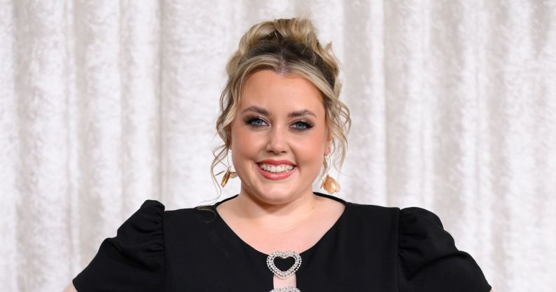Charley Marlowe poses and smiles while wearing a black dress. She is stood against a white curtain background.