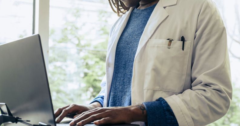 A doctor, face not pictured, typing on a laptop.