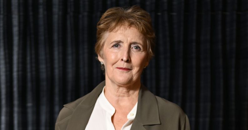 Fiona Shaw in a grey jacket, white shirt, against a black background.