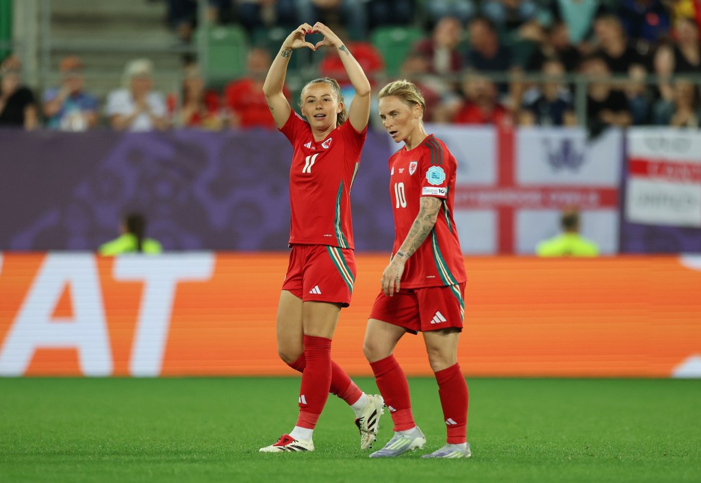 Hannah Cain of Wales celebrates scoring her team's first goal during the UEFA Women's EURO 2025 Group D match between England and Wales. She holds up a hand heart to the crowd.