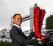 Johannes Radebe in front of London bridge and a black taxi holding up Kinky Boots' red lace hup knee-high boots