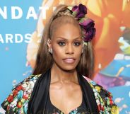 Laverne Cox in a multi-coloured floral jacket with matching hairpiece, stood against a floral, multi-coloured background.