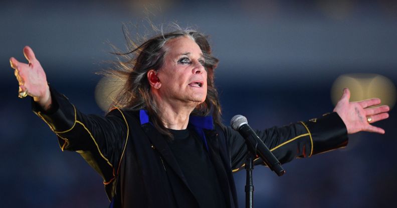 Ozzy Osbourne holds open his arms and looks upward while standing in front of a microphone performing.