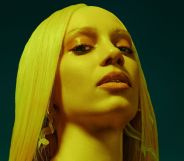 Pop singer Agnes poses in a blonde wig. She is showered in a yellow light, against a blue-black background.