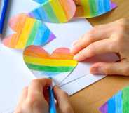 A girl colours a Heart cut out of paper in the colours of the LGBTQ Pride flag.