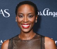 The Pitt star Tracy Ifeachor beams while stood against a blue and white background. She is wearing a see-through vest top and striking red lipstick.