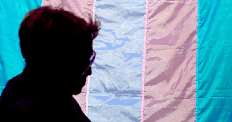 A silhouette in front of a trans flag.