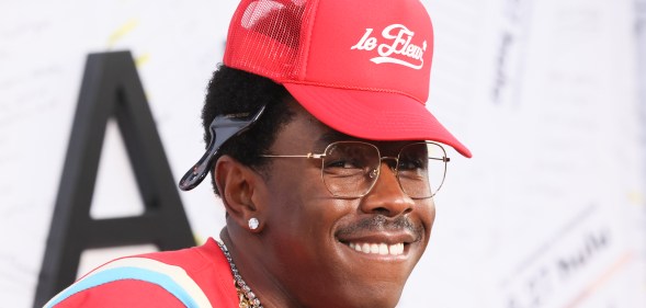 Tyler the Creator on a red carpet with a red hat, t-shirt and chains