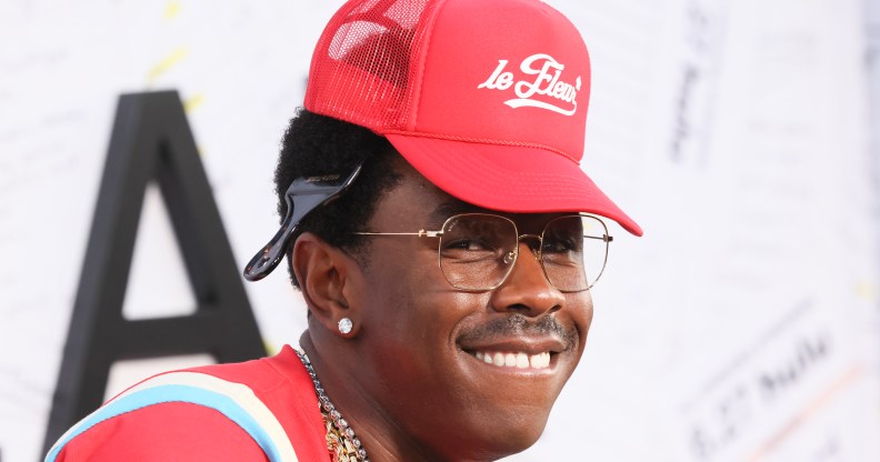 Tyler the Creator on a red carpet with a red hat, t-shirt and chains