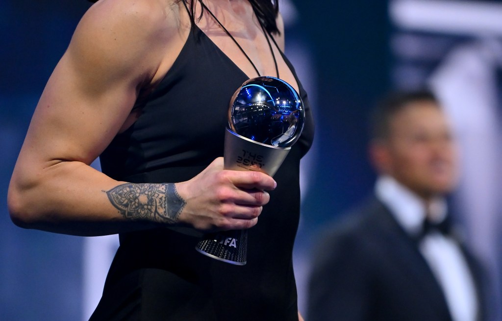 Lucy Bronze of FC Barcelona and England carries her trophy after being named in the FIFA FIFPRO Women's World 11 2022. Her right hand holding the trophy has a tattoo across her forearm and wrist.