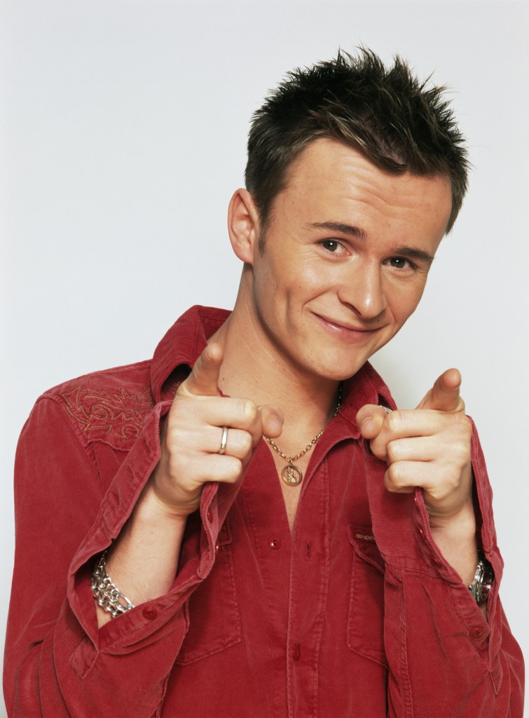British pop singer Jon Lee in 2000. He's wearing an oversized red shirt with a gold necklace, silver bracelets and silver watch. He's got brown, short spiky hair