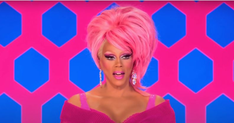 RuPaul on the Drag Rac judging panel in a pink outfit and pink wig with her mouth open.