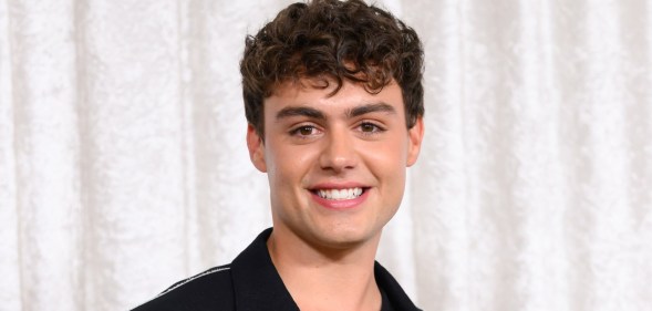 Bradley Riches smiling at the camera. He's wearing a black suit and standing in front of a white curtain