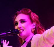 Chappell Roan performing, singing into the mic while wearng a white shirt and leafy gold earings.