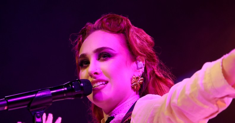 Chappell Roan performing, singing into the mic while wearng a white shirt and leafy gold earings.