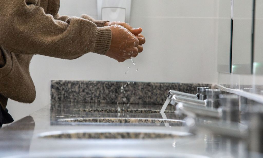 A person in a public bathroom washing their hands.