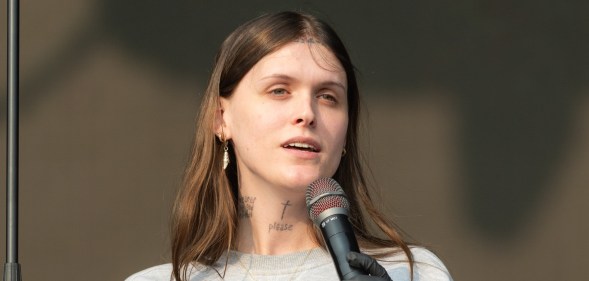Ethel Cain performs during All Points East Festival. She's holding the mic, wearing a grey sweatshirt with a gold cross necklace.