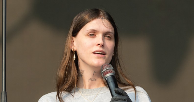 Ethel Cain performs during All Points East Festival. She's holding the mic, wearing a grey sweatshirt with a gold cross necklace.