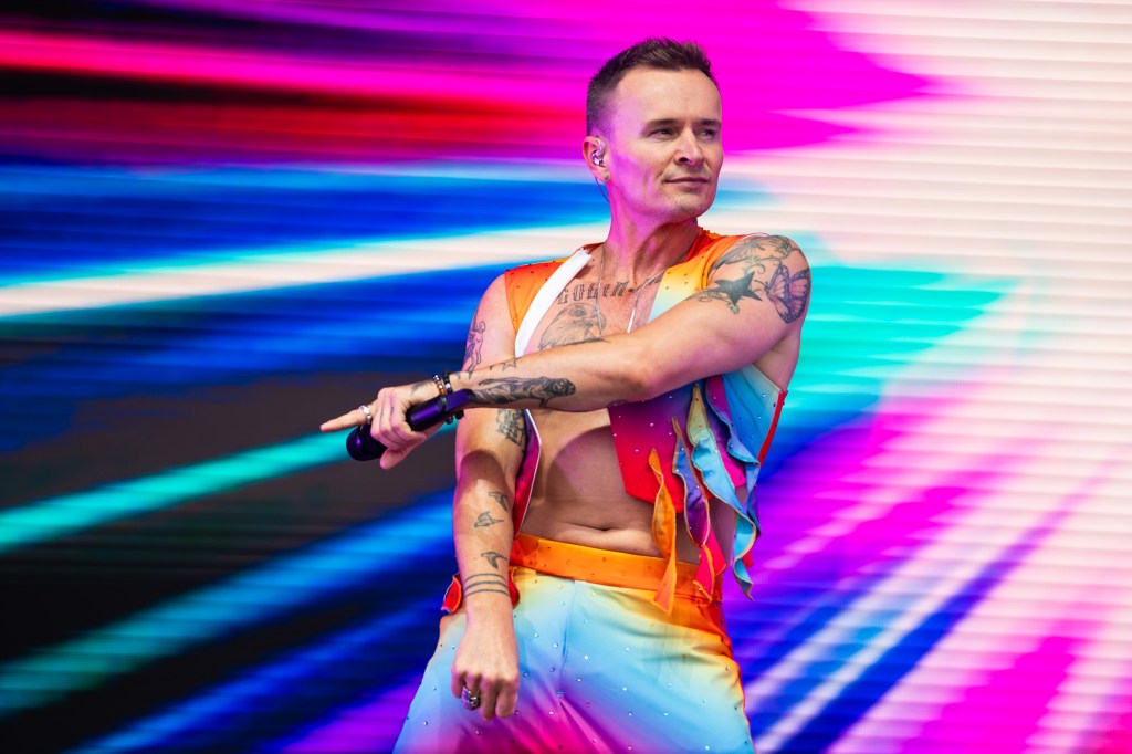 Jon Lee of S Club performs on stage during "Fabuloso Day 2 - Pride In The Park". He's wearing a rainbow open shirt and matching trousers.