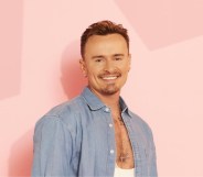 Jon Lee in a light blue denim shirt and white vest. He's standing against a pink star background.