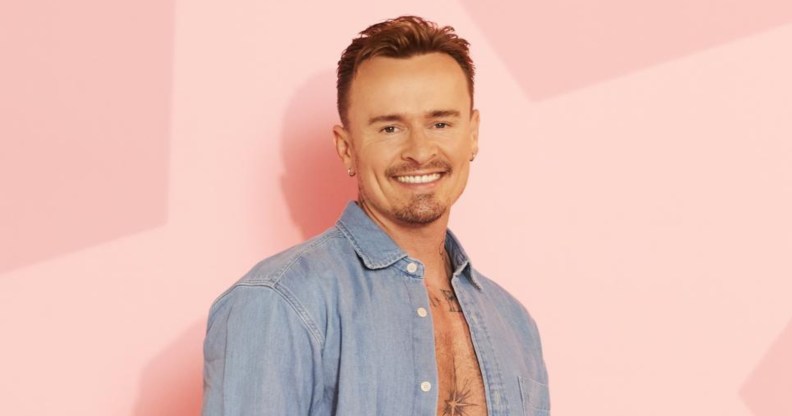 Jon Lee in a light blue denim shirt and white vest. He's standing against a pink star background.