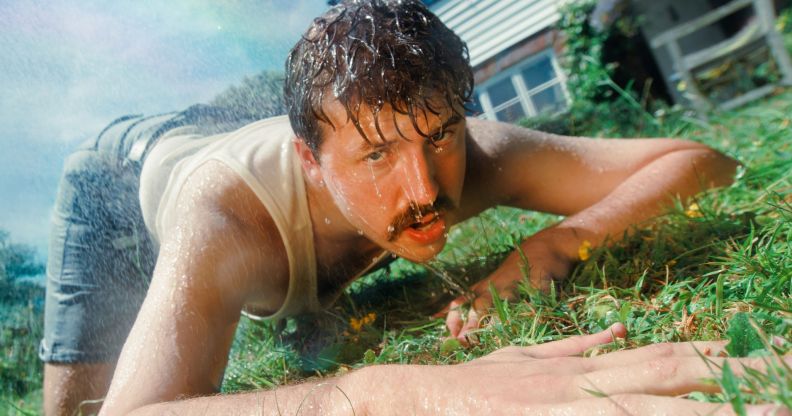 Kai Bosch lays on the grass wearing a white vest and blue jean shorts. He is dripping wet.