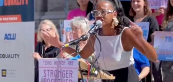 Activist Kimiya Factory speaks next to a sign that reads "stronger together"