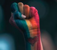 A person's fist in LGBTQ+ Pride colours.
