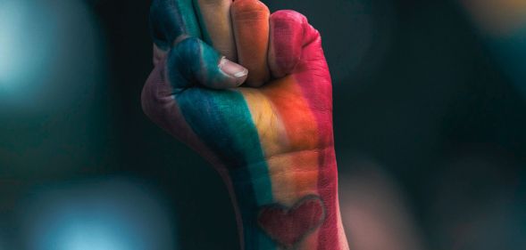 A person's fist in LGBTQ+ Pride colours.
