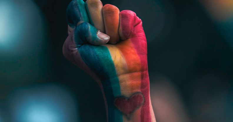 A person's fist in LGBTQ+ Pride colours.