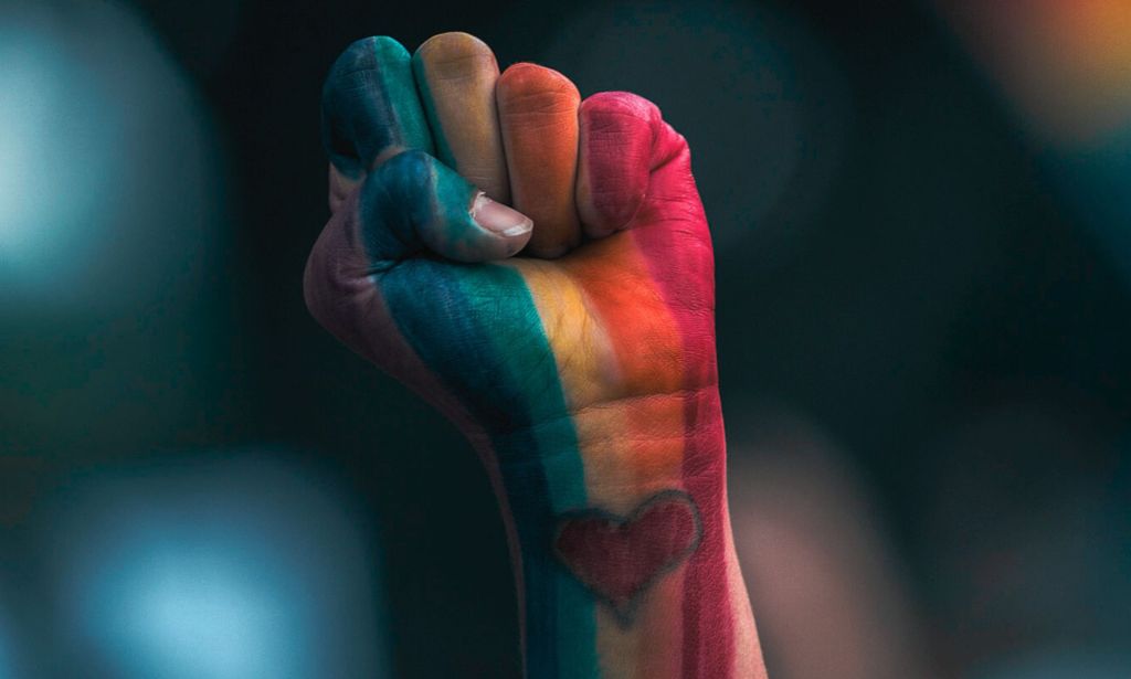 A person's fist in LGBTQ+ Pride colours.
