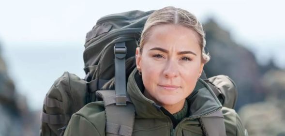 Lucy Spraggan poses and looks stern while wearing military gear and a back pack.