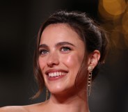 Margaret Qualley arrives for the screening of the film "Honey Don't!" at the 78th edition of the Cannes Film Festival in Cannes. Close-up photo of Margaret smiling, wearing floral dangly earings.