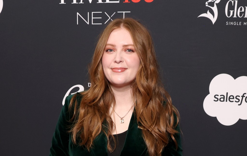 Alice Oseman attends the 2024. They've got long ginger hair goin over their dark green velvet suit.