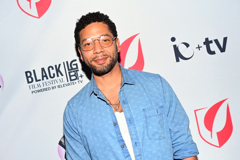 Jussie Smollett wearing a denim jacket over a white vest. He's also wearing tinted silver glasses.