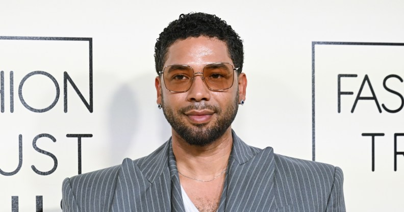 Jussie Smollett in a grey pinstruoe suit. He's got brown tinted glasses on.