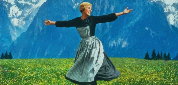 The Sound of Music still: Maria in a long dark top with striped dress dancing in a yellow flower meadow in front of mountains