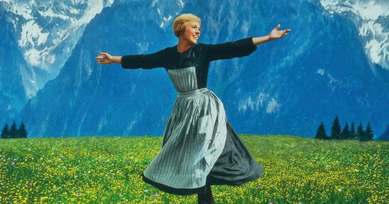 The Sound of Music still: Maria in a long dark top with striped dress dancing in a yellow flower meadow in front of mountains