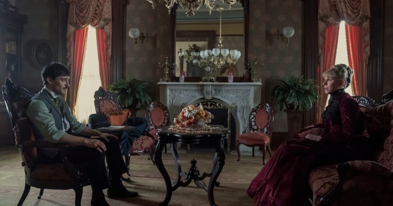 Oscar and Agnes are sat in an ornate living room on chairs opposite eachother, a pot of dying flowers in between them.