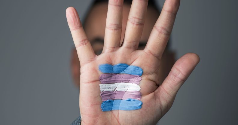 A person putting their hand up with trans flag colours on it.