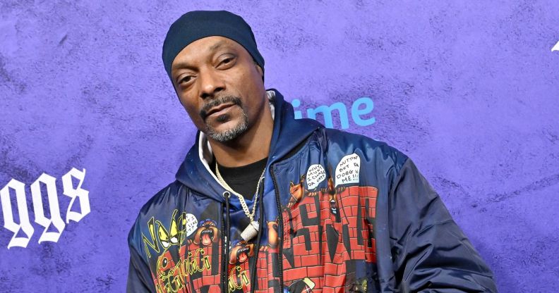 Snoop Dog in a blue yello and red denim jacket at a premiere with a purple background behind him.