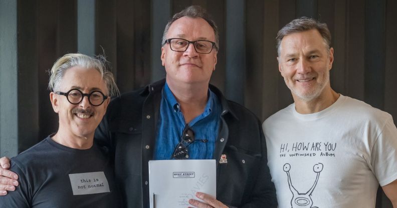 A photo of Russell T Davies (C) smiling and holding a script for Tip Toe, with his arm around actors Alan Cumming (L) and David Morrissey.