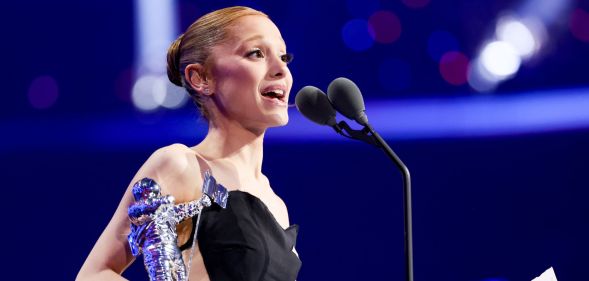 Ariana Grande holding a moon person statue and speaking into a microphone as she accepts a video music award.