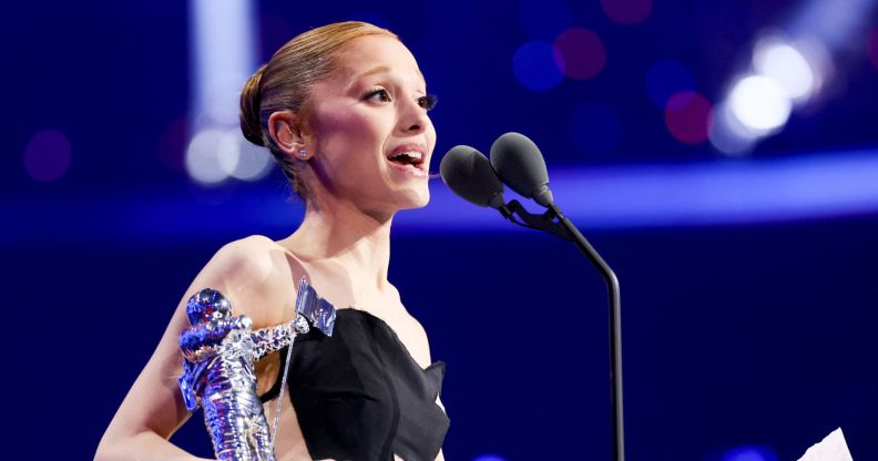 Ariana Grande holding a moon person statue and speaking into a microphone as she accepts a video music award.