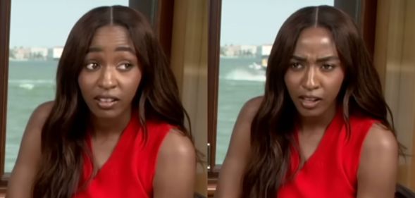 Ayo Edebiri looking shocked in a press junket. She is wearing a red top with her hair over her right shoulder.