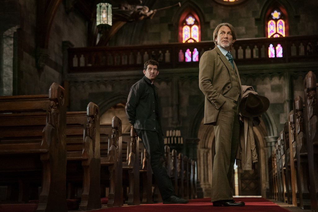Wake Up Dead Man: A Knives Out Mystery still: Daniel Craig standing in a church to the right of frame with Josh O'Connor behind him.