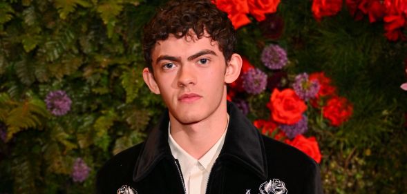 Joe Locke poses in a black jacket and white shirt against a flowery background.
